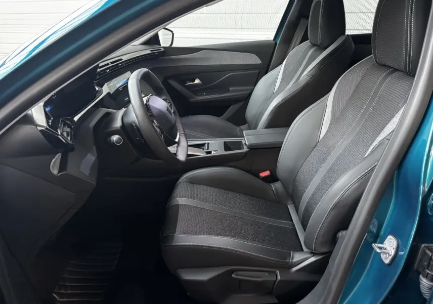 Vue intérieure côté conducteur de la Peugeot 308 Hybrid bleu, avec sièges tissu et cuir et volant multifonctions cuir.