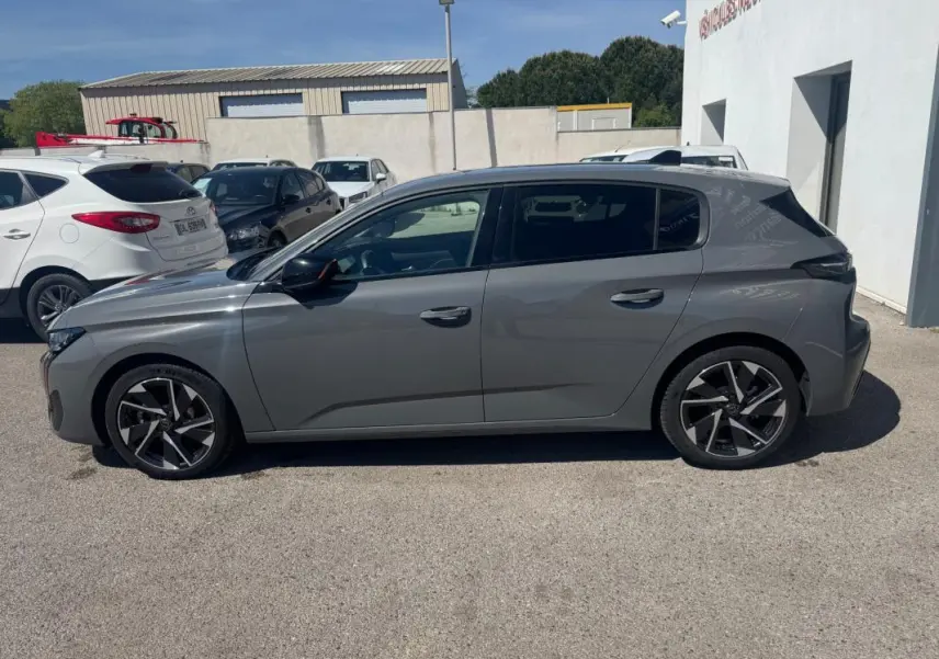 Profil côté gauche de la Peugeot 308 Hybrid gris 2025 avec jantes alliage 17 pouces, stationnée en extérieur.