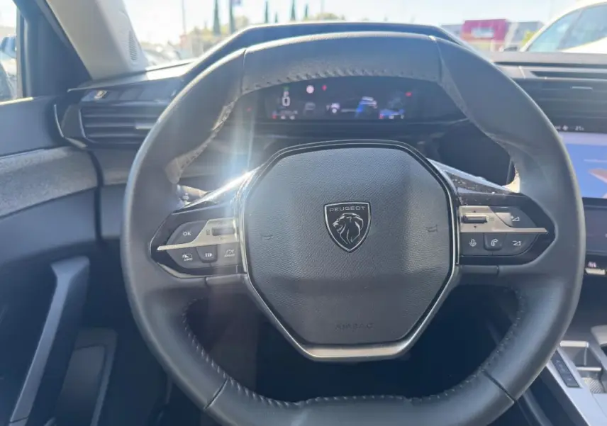 Vue rapprochée du volant cuir noir du Peugeot 308 Hybrid 136 e-DCS6 Allure avec commandes intégrées et tableau de bord numérique.