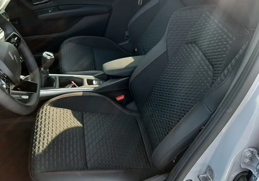 Vue intérieure côté conducteur de la Renault Clio VI TCE 115CH TECHNO 2026, sièges noirs en tissu et cuir avec surpiqûres rouges.