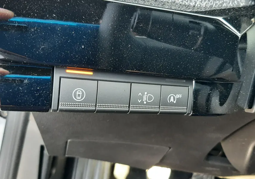 Gros plan sur les boutons de commande sous le tableau de bord d'une Renault Clio VI gris Rafale, avec témoin orange allumé.