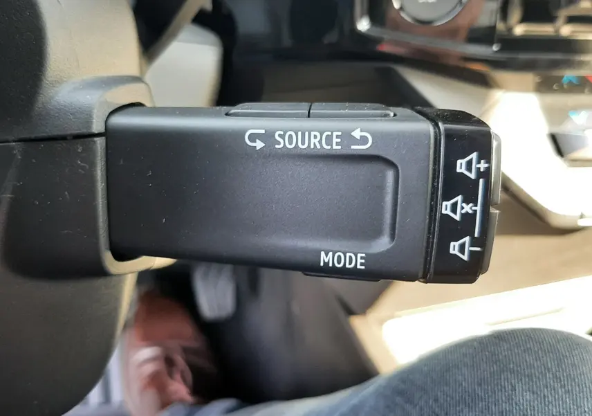 Gros plan sur la commande au volant droite de la Renault Clio VI gris Rafale, avec boutons source et mode visibles.