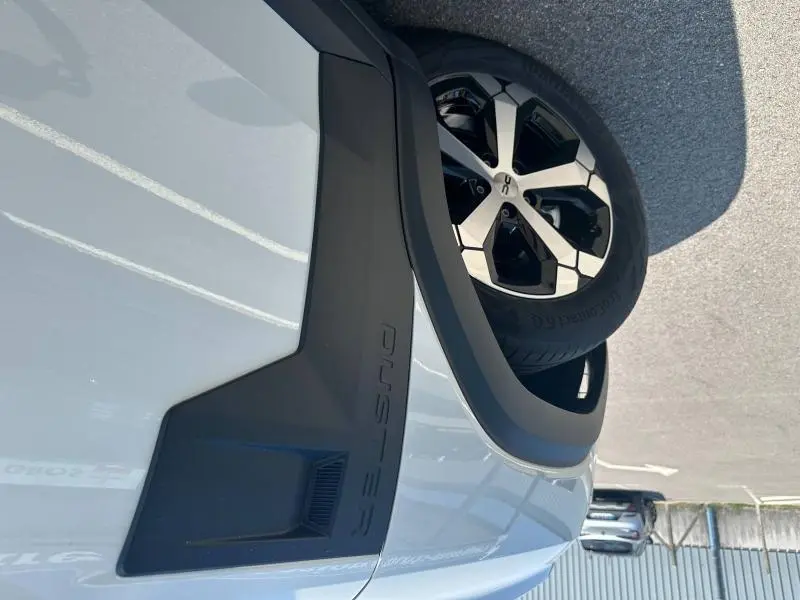 Gros plan sur l'aile avant droite blanche du Dacia Duster 2025 avec jante alu et logo Duster en relief noir.