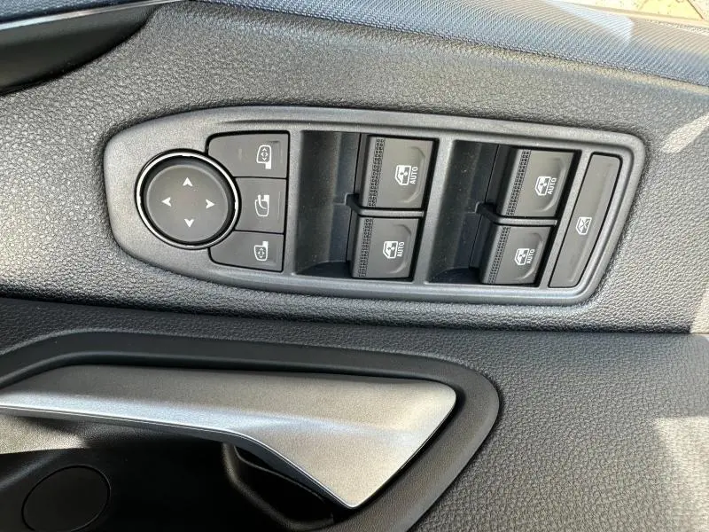 Gros plan sur les commandes des vitres et rétroviseurs côté conducteur du Dacia Duster blanc 2025.