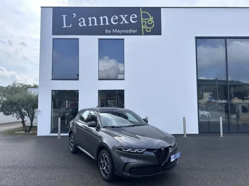 Alfa Romeo Tonale gris foncé métal en 3/4 avant droit devant un bâtiment blanc avec enseigne L'annexe by Meynadier.