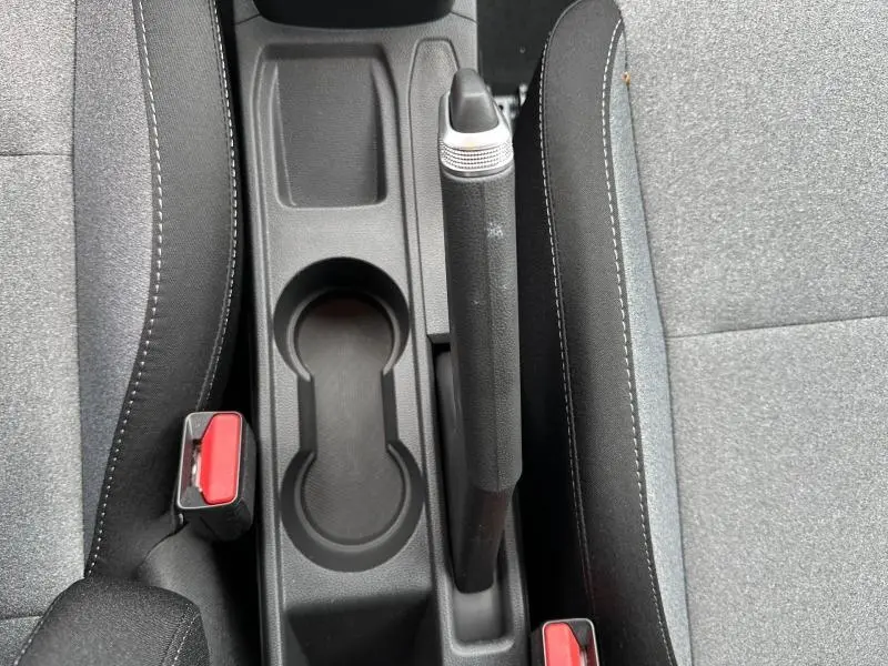 Vue plongeante sur le frein à main manuel et porte-gobelets entre les sièges tissu gris de la Renault Clio 2025.