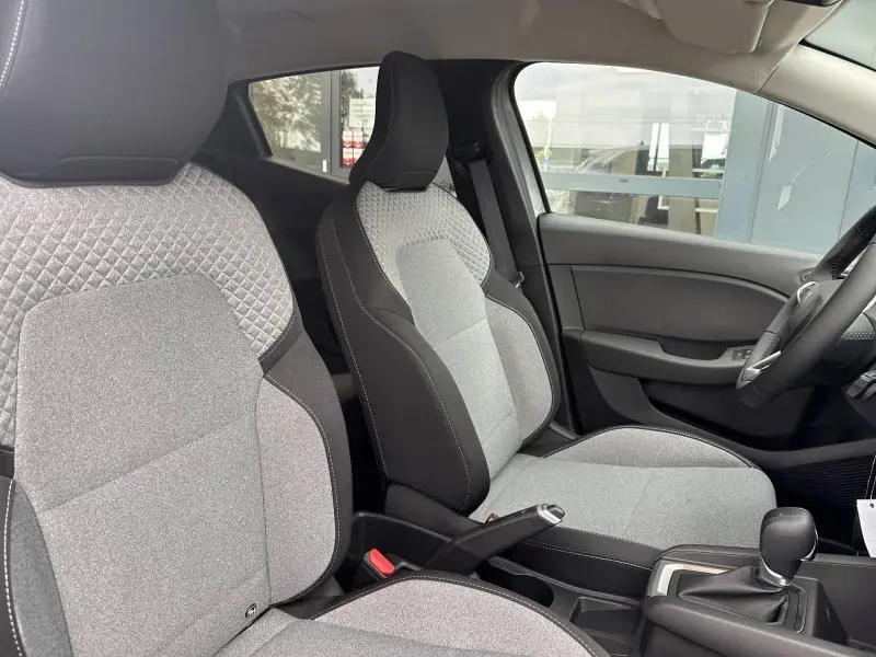 Intérieur avant de la Renault Clio 2025, sièges en textile gris à motif 3D, volant multifonction et boîte manuelle visibles.