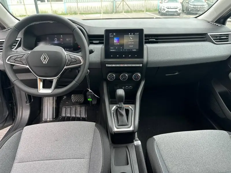 Vue intérieure avant de la Renault Clio 2025, tableau de bord gris avec écran tactile central et volant multifonction.