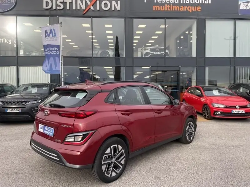 Vue 3/4 arrière droite d'un Hyundai Kona électrique rouge métal 2021, avec jantes spécifiques et feux arrière distinctifs.