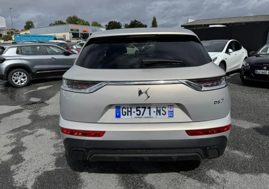 Vue arrière d'un DS7 Crossback gris métallisé avec feux arrière 3D et lunette arrière teintée sur parking.