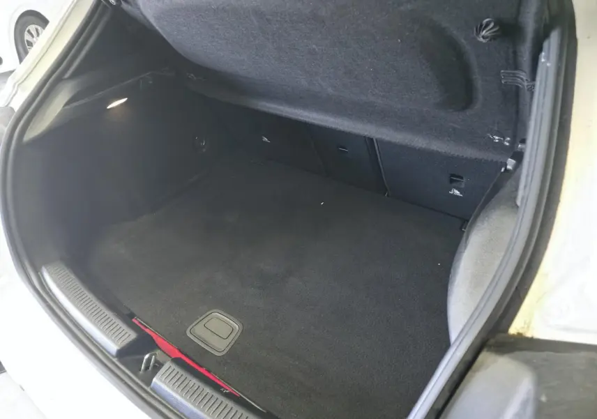 Coffre ouvert vu de l'arrière d'une Mercedes Classe A 160 Style Line blanche, intérieur noir et tapis propre.