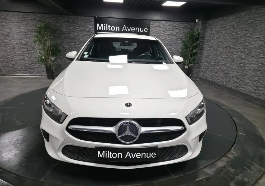 Vue frontale d'une Mercedes Classe A 160 Style Line blanche avec calandre diamant et logo central dans un showroom.