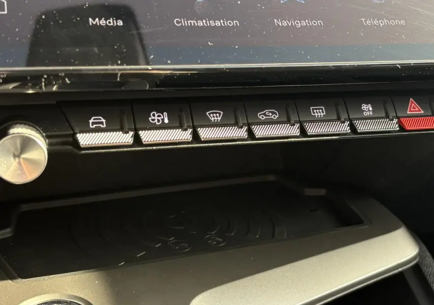 Gros plan sur la console centrale de la Peugeot 308 Hybrid 2025, montrant les boutons de commande et le chargeur à induction.