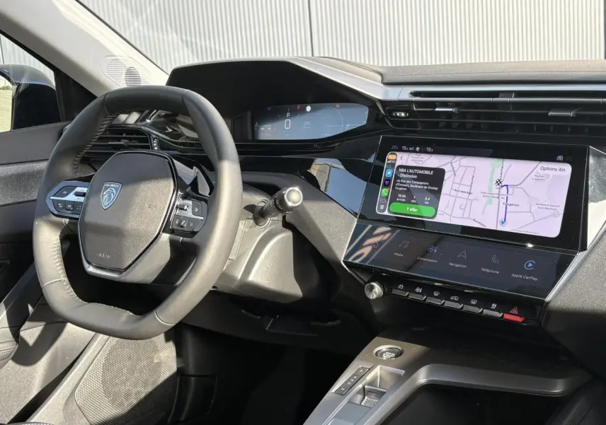 Vue intérieure du poste de conduite de la Peugeot 308 Hybrid 2025, volant cuir et écran tactile de navigation Apple CarPlay.