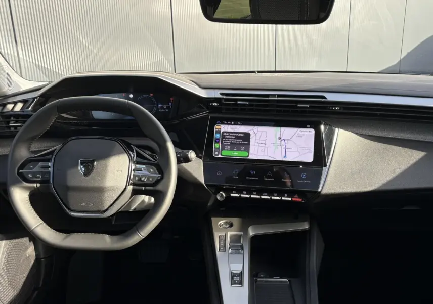 Vue intérieure frontale du poste de conduite de la Peugeot 308 Hybrid 2025 avec écran tactile et volant cuir noir.