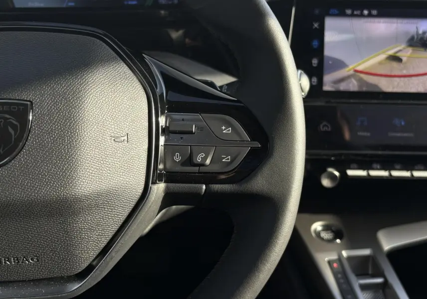 Gros plan sur le volant en cuir noir de la Peugeot 308 Hybrid 2025 avec commandes intégrées et écran tactile affichant la caméra 360°.