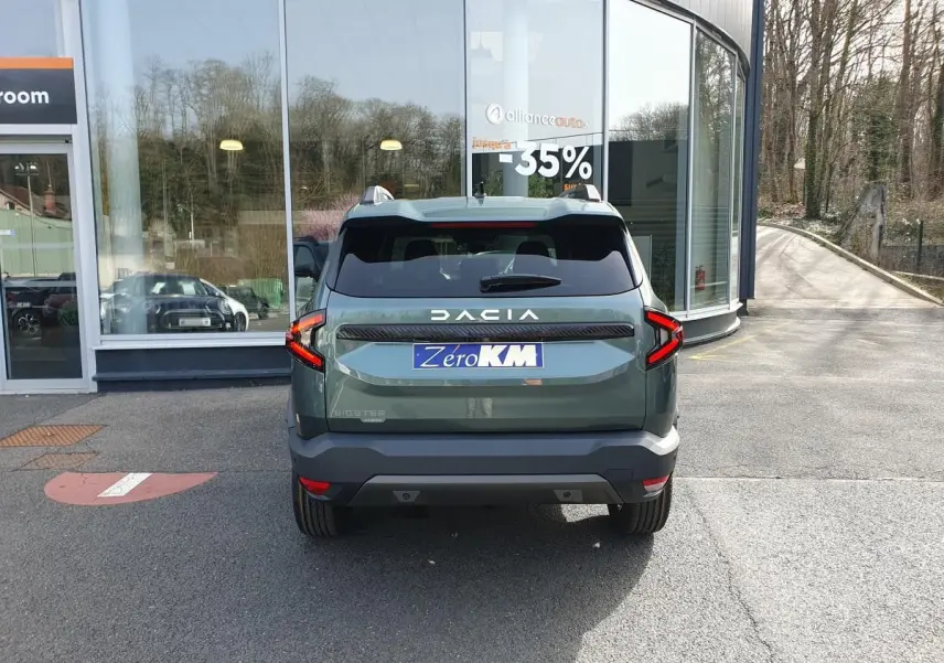 Vue arrière du Dacia Bigster vert cèdre avec toit panoramique et feux LED distinctifs, stationné devant une vitrine.