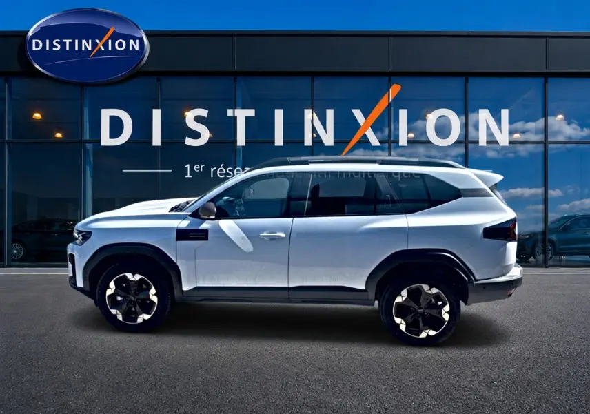 Vue de profil côté gauche du Dacia Bigster blanc 2026 avec jantes alu et barres de toit, devant une vitrine Distinxion.