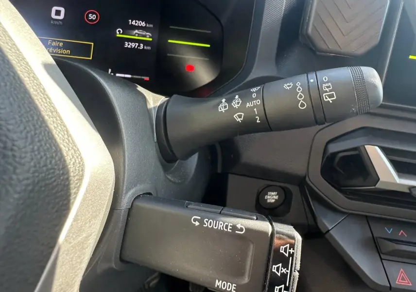 Gros plan sur la commande multifonction et le tableau de bord numérique du Dacia Duster 2025, intérieur noir.