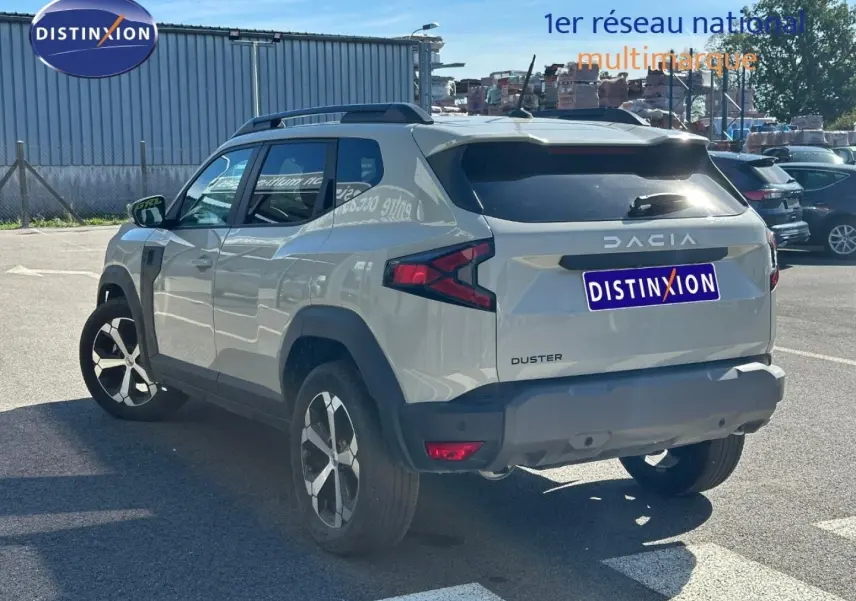 Vue 3/4 arrière droite du Dacia Duster 2025 couleur Sandstone avec barres de toit et jantes alu distinctives.