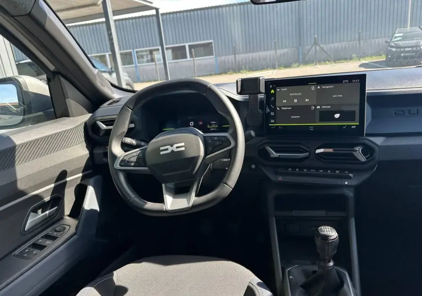 Vue intérieure côté conducteur du Dacia Duster 2025 avec volant multifonction, écran tactile et levier de vitesse manuel.