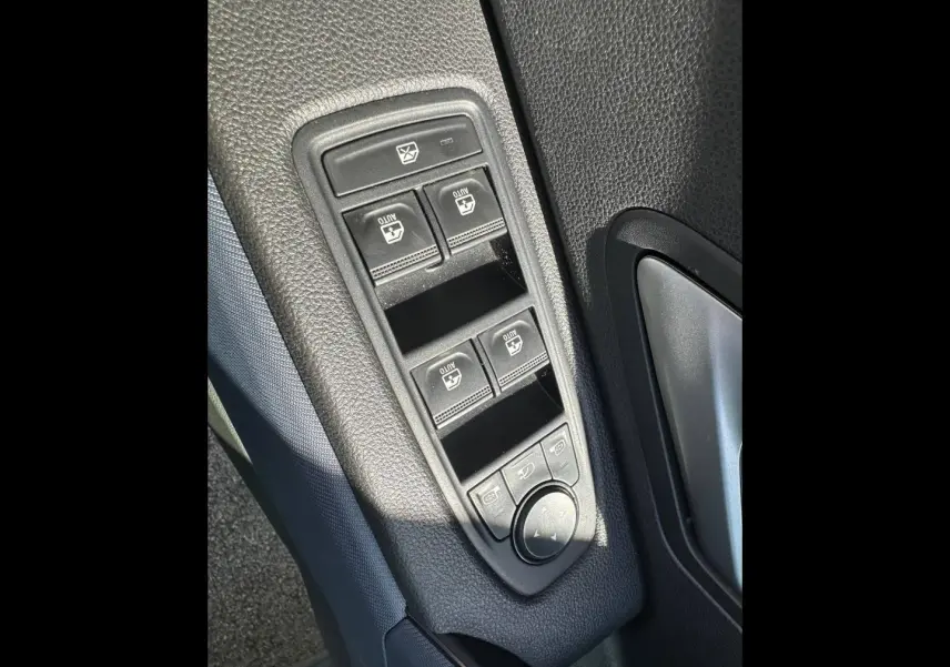 Vue rapprochée des commandes de lève-vitres et réglage des rétroviseurs sur la porte côté conducteur du Dacia Duster Sandstone.