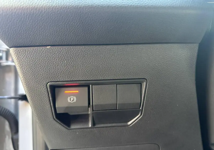 Détail du bouton de frein de stationnement électronique allumé sur le tableau de bord noir du Dacia Duster 2025.