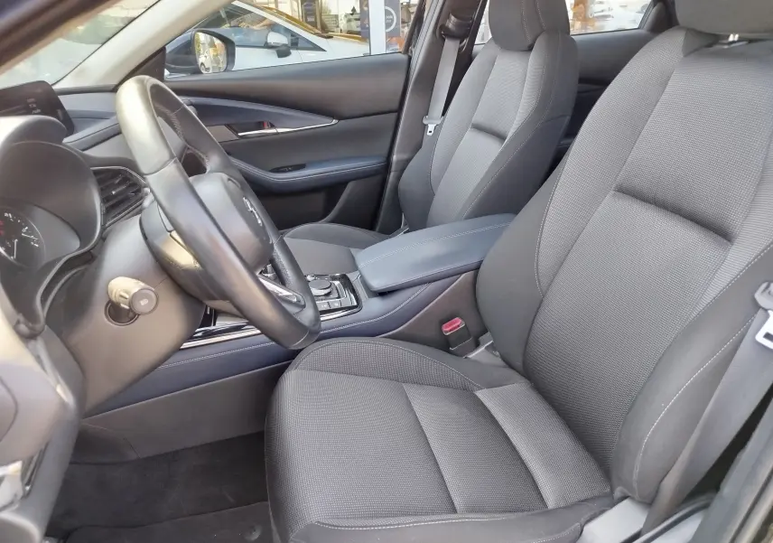 Vue intérieure côté conducteur du Mazda CX-30 2020, sièges tissu noir et tableau de bord moderne avec volant cuir.