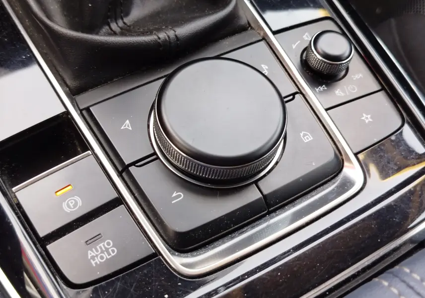 Gros plan sur la molette de commande centrale noire et les boutons environnants dans l'habitacle du Mazda CX-30 noir.