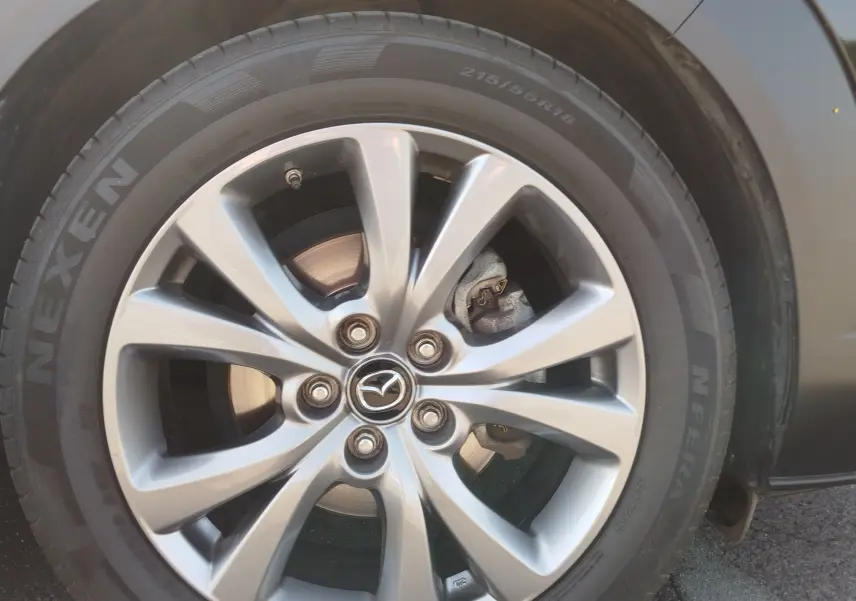 Gros plan sur la jante alliage argentée et pneu Nexen d'un Mazda CX-30 noir, mettant en valeur le logo Mazda central.