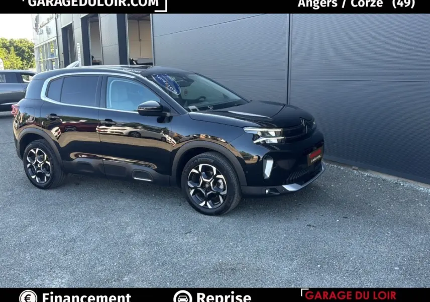Vue 3/4 avant droit d'un SUV Citroën C5 Aircross noir brillant garé devant un mur gris.