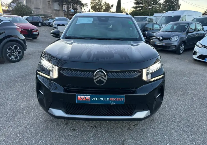 Vue de face d'une Citroën C3 noire 2025 avec phares allumés, calandre moderne et barres de toit visibles.