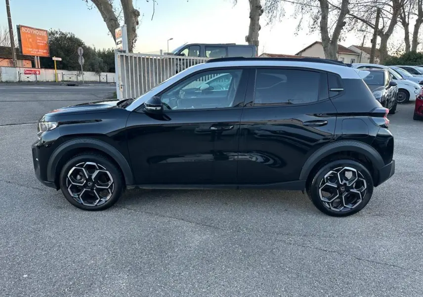 Profil côté gauche d'une Citroën C3 noire 2025 avec toit blanc et jantes alliage 17 pouces, stationnée en extérieur.