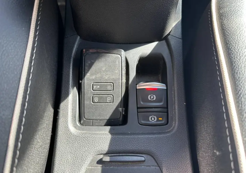 Gros plan sur la console centrale noire de la Renault Clio 1.0 Eco-G 100ch Techno avec commandes électroniques et accoudoir.
