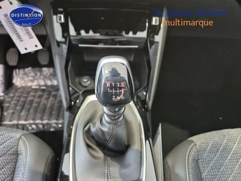 Le levier de vitesses manuel de la Peugeot 208 gris Artense, vu de dessus entre les sièges avant.