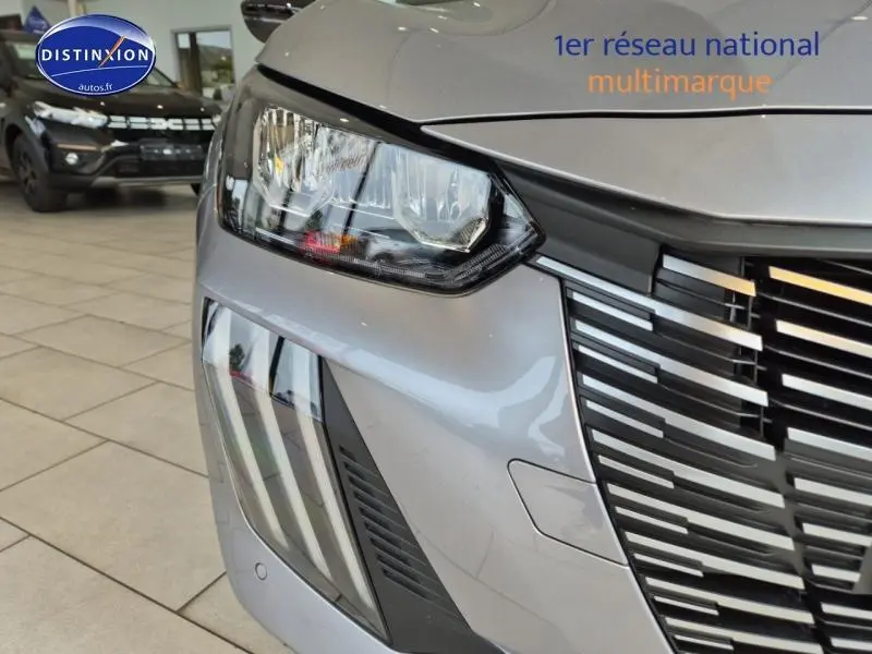 Gros plan sur le phare avant gauche et la calandre noire de la Peugeot 208 gris Artense en concession