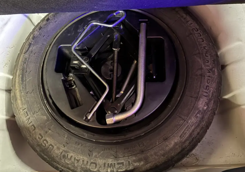 Pneu de secours noir avec outils de changement rangés au centre, vue plongeante dans le coffre d'une FIAT 500 blanche.