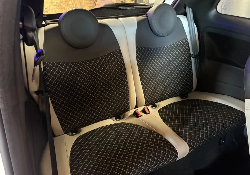 Vue intérieure sur les sièges arrière en tissu noir à motifs blancs de la Fiat 500 blanche, version DolceVita 2021.