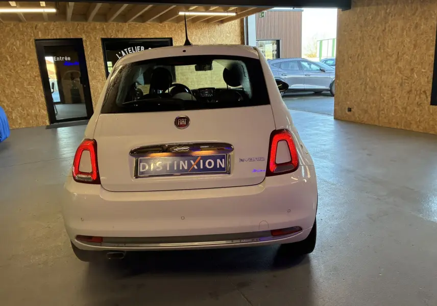Vue arrière d'une FIAT 500 blanche de 2021, avec feux allumés et badge Hybrid visible dans un garage.