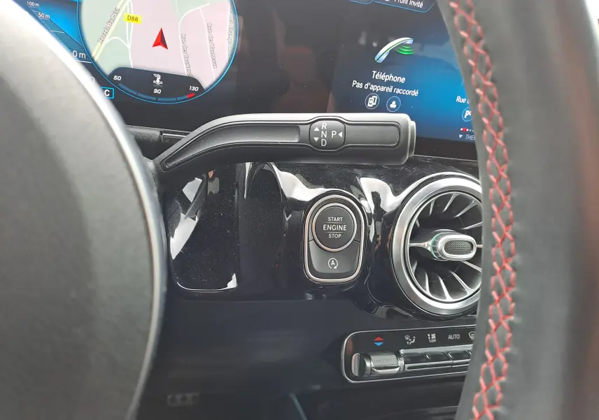 Détail intérieur montrant le bouton start/stop et la commande de boîte automatique sur fond noir brillant d'une Mercedes Classe B gris foncé.