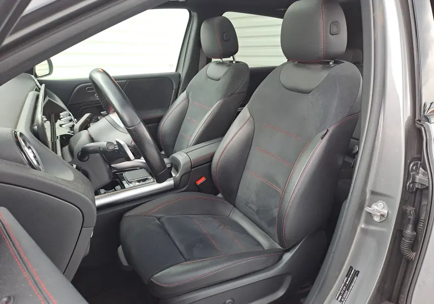 Vue intérieure côté conducteur d'une Mercedes Classe B 1.3i AMG Line 2019, sièges noirs avec surpiqûres rouges.