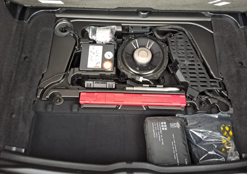 Vue plongeante sur le compartiment de rangement sous coffre d'une Mercedes Classe B gris foncé, avec kit de réparation et outils visibles.