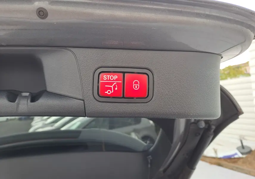 Gros plan sur les boutons rouges de fermeture et arrêt du hayon d’un Mercedes Classe B gris foncé métallisé.