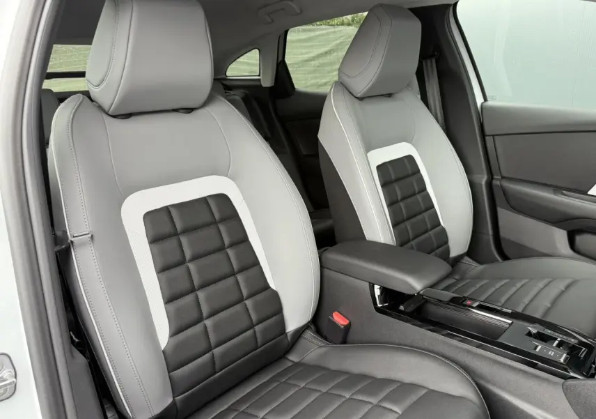 Vue intérieure des sièges avant gris clair et noir à motifs carrés du Citroën C4 NV Hybrid 2025 avec accoudoir central.