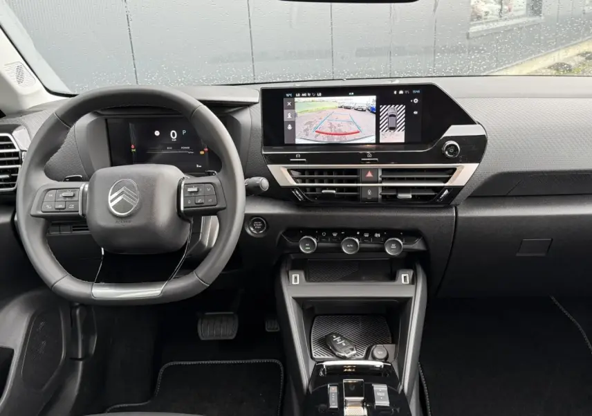 Vue frontale de l'habitacle noir du Citroën C4 2025, avec volant multifonction et écran tactile affichant la caméra de recul.