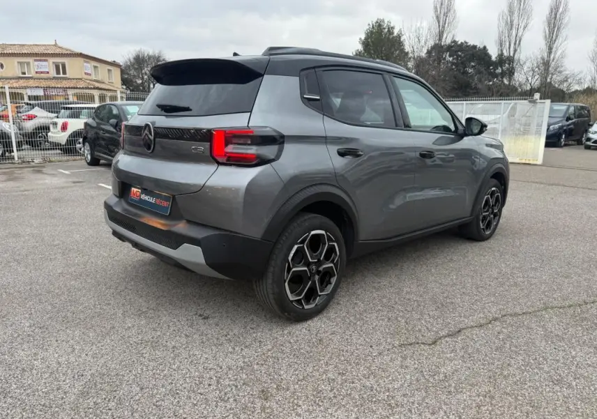 Vue 3/4 arrière droite d'une Citroën C3 gris métallisé avec jantes alliage 17 pouces et barres de toit visibles.