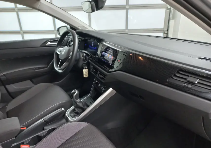Intérieur de la Volkswagen Polo 2024 en vue côté conducteur, tableau de bord noir avec écran tactile et boîte manuelle.