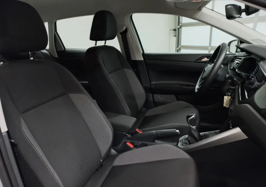 Intérieur de la Volkswagen Polo 2024 en vue latérale côté conducteur, sièges noirs et levier de vitesses manuel visible.