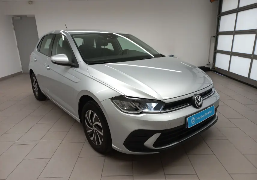 Volkswagen Polo 2024 reflet d'argent vue 3/4 avant droit en intérieur avec phares allumés et caméra de recul.