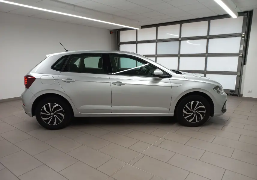 Profil côté gauche d'une Volkswagen Polo 2024 argentée, avec jantes stylisées et caméra de recul visible au-dessus du pare-chocs arrière.
